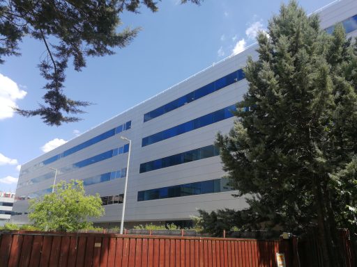 Edificio de Atos en Madrid visto a través de frondosos árboles, con láminas de tratamiento solar en sus ventanas