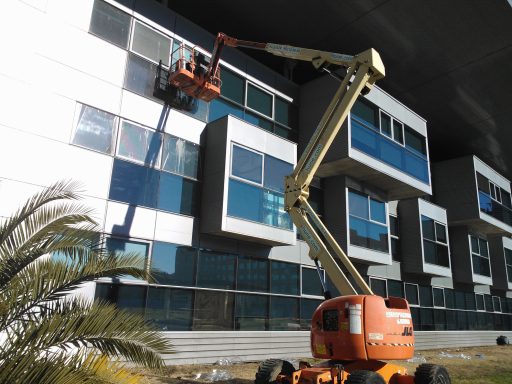  Plataforma elevadora con una persona instalando lámina en una ventana alta. Descubre nuestras Laminas Tratamiento Cristales LTC.