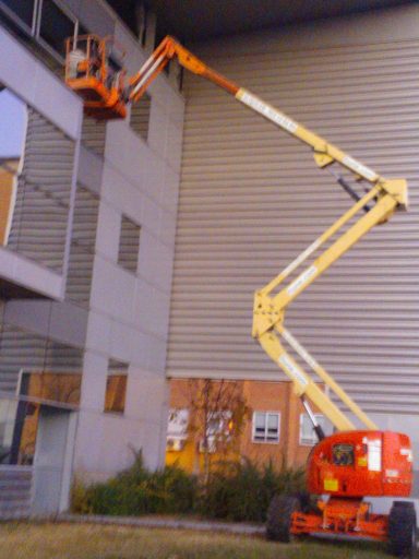 Persona en plataforma elevadora instalando láminas en ventana alta.