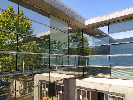 Edificio moderno con ventanas tratadas con láminas reflectantes, rodeado de árboles bajo un cielo despejado.