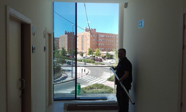 Un técnico se prepara para instalar láminas de tratamiento en la puerta de vidrio de un edificio, mejorando la eficiencia y la privacidad